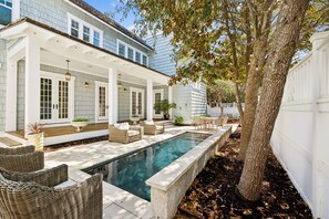 A pool area with wicker furniture, a pergola, and a large tree.