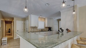 Une cuisine spacieuse avec des meubles blancs, un grand îlot central et des luminaires suspendus.