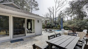 Un patio couvert avec une piscine, des sièges d’extérieur et une vue sur les arbres environnants.