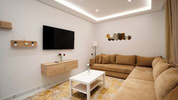 A modern living room with a flat-screen TV, a wooden cabinet, a white coffee table, and a beige sofa.