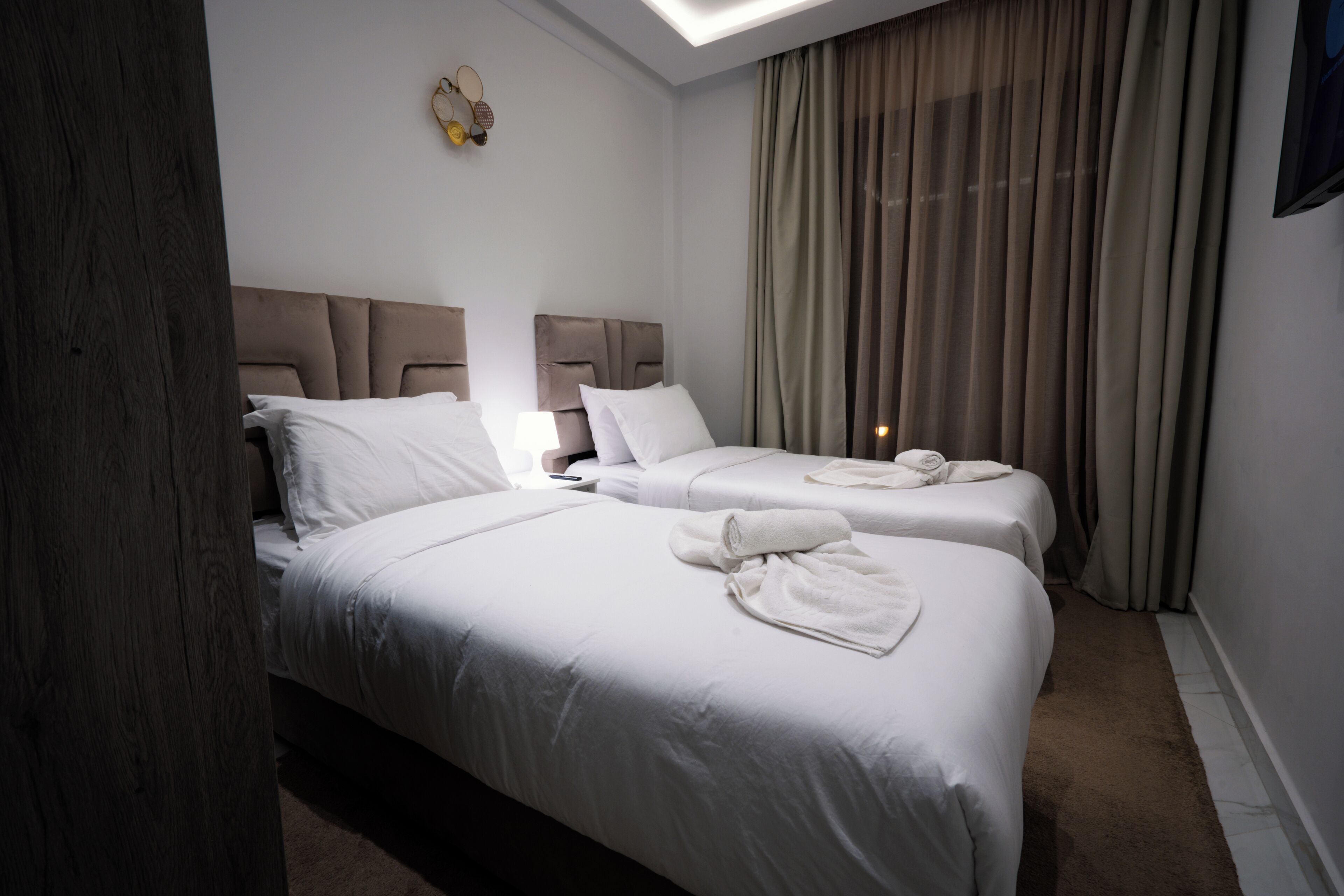 Une chambre d’hôtel avec deux lits, un pilier en bois, un luminaire au plafond et une fenêtre avec des rideaux.