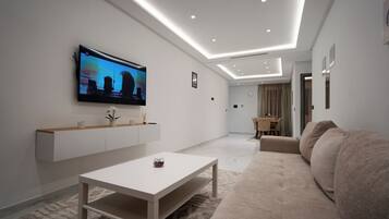 Una sala de estar moderna con un televisor de pantalla plana montado en la pared, una mesa de centro blanca y un sofá color beige.