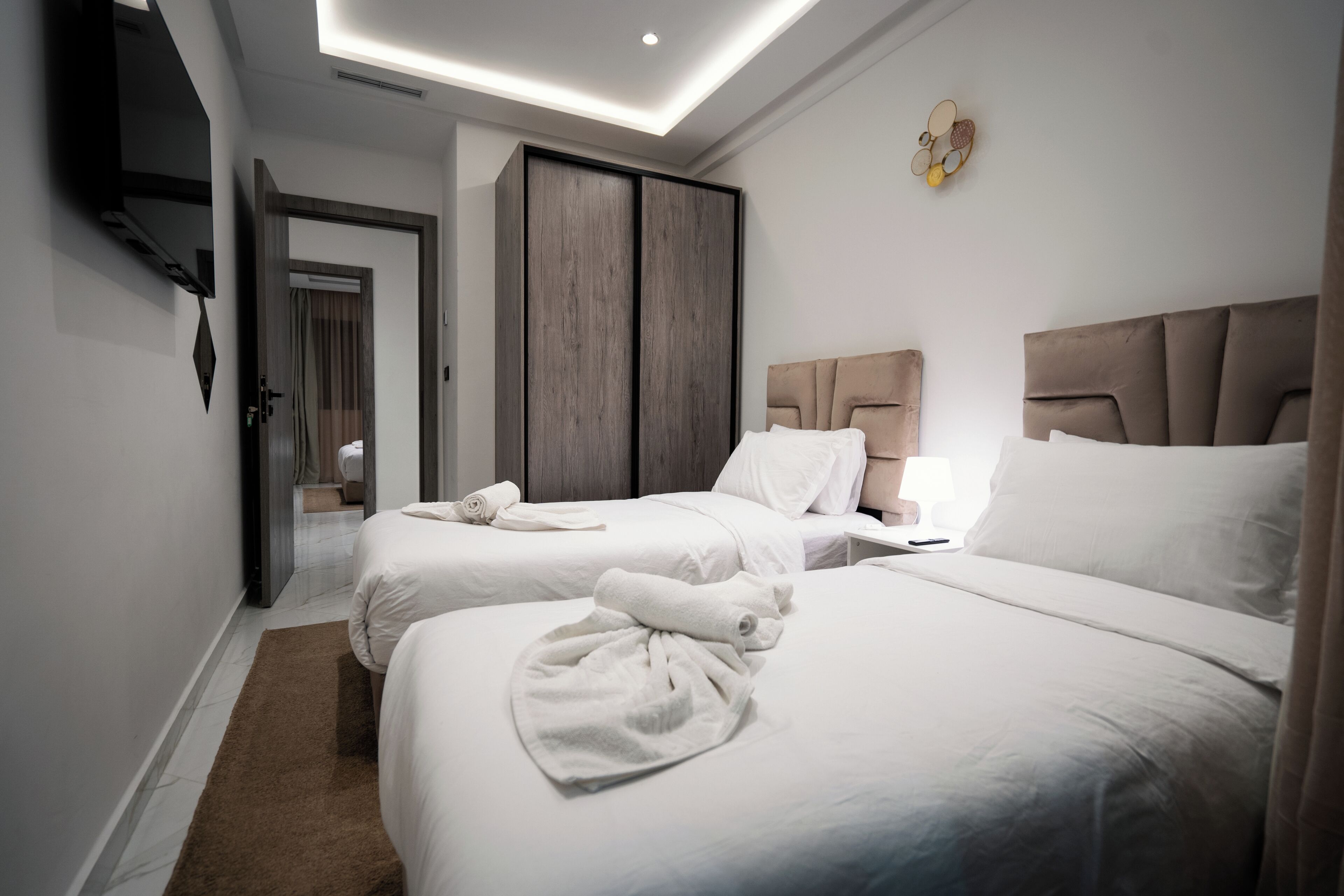 A hotel room with two beds, a wardrobe, a flat-screen TV, and a ceiling light.