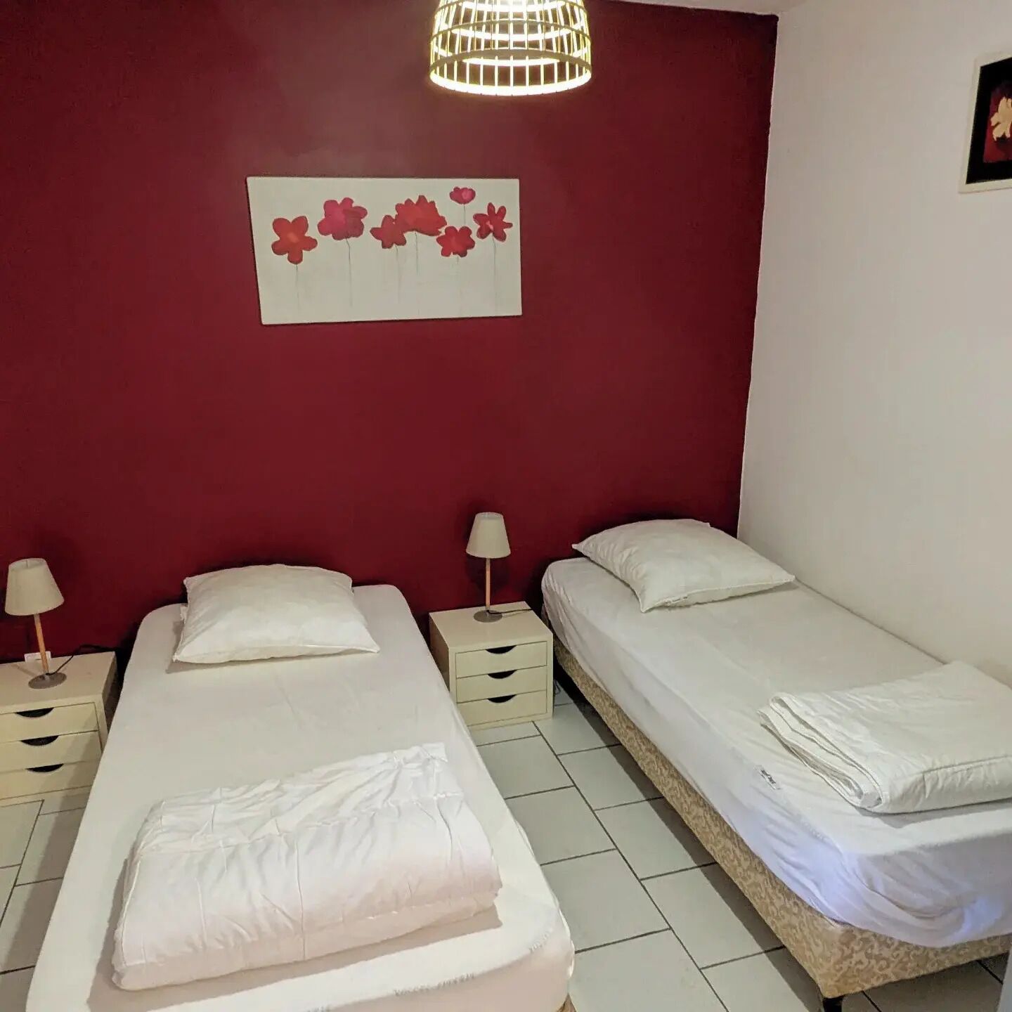 Une chambre avec deux lits, un mur d’accent rouge, une décoration murale représentant des fleurs et un luminaire suspendu.