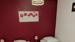A room with two beds, a red accent wall, a decorative flower wall art, and a hanging light fixture.