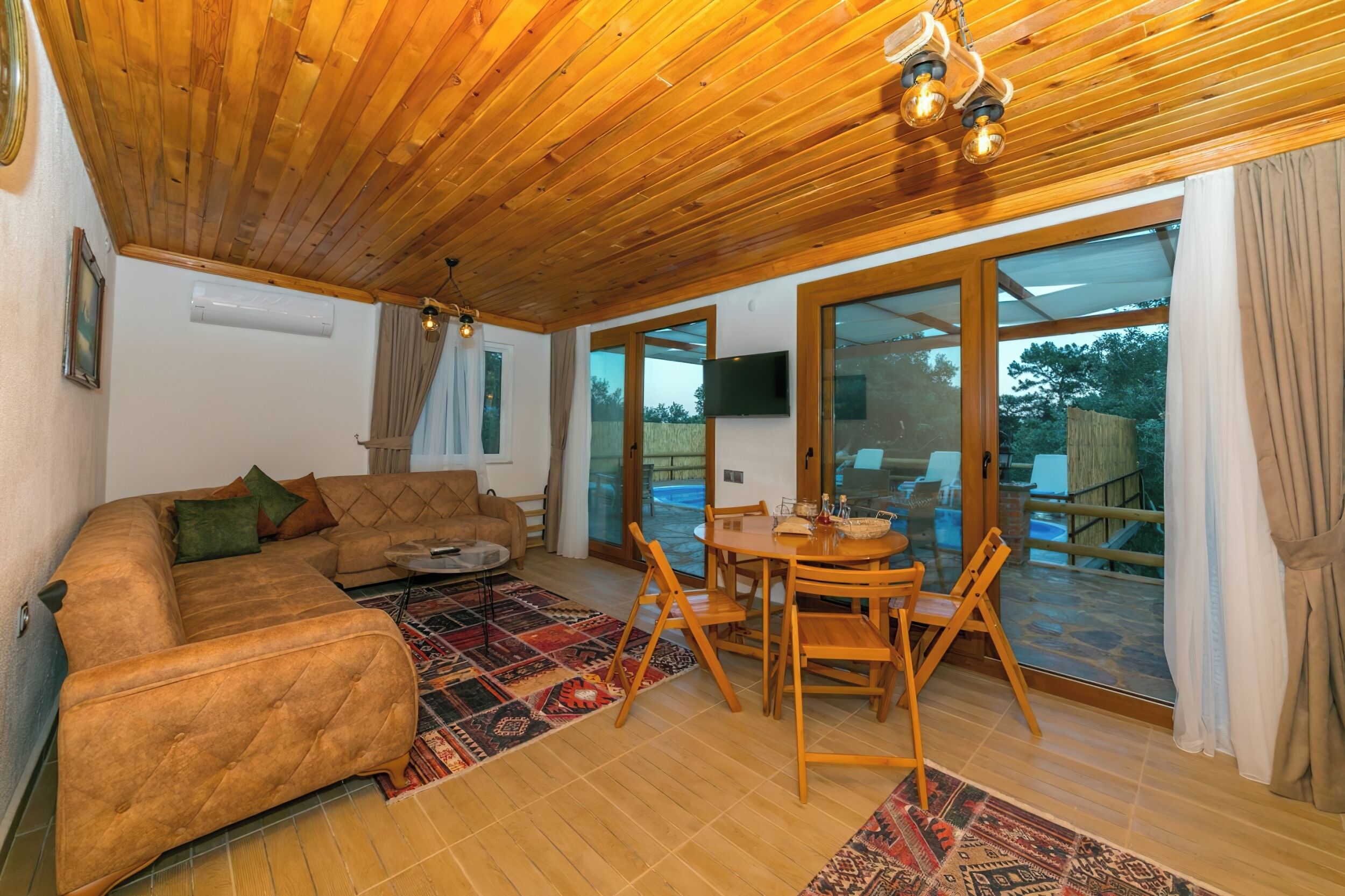Una sala de estar acogedora con techo de madera, un sofá modular, una mesa de centro y un comedor con sillas y una mesa.