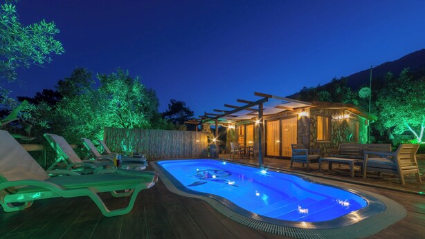 En pool med solstolar och en överbyggd sittplats i skymningen.