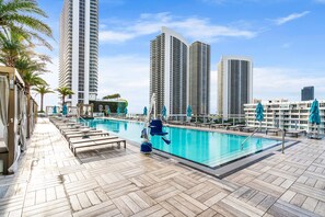 A rooftop pool area with lounge chairs and umbrellas, surrounded by tall buildings. - 2BR Ocean Penthouse: Private Terrace & Hot Tub (Hollywood)
