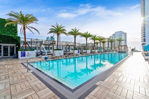 A rooftop pool with palm trees, lounge chairs, and a view of the city skyline. - 2BR Ocean Penthouse: Private Terrace & Hot Tub (Hollywood)