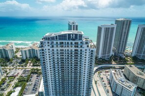 A high-rise hotel with a prominent rooftop sign, surrounded by other tall buildings and a beach view. - 2BR Ocean Penthouse: Private Terrace & Hot Tub (Hollywood)