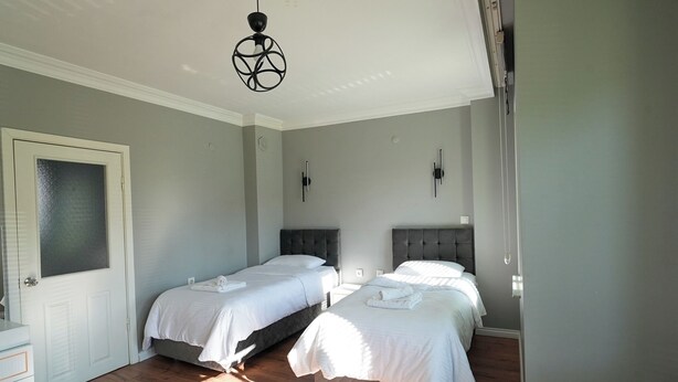 A bedroom with two beds, a white door, a small bedside table, and a hanging light fixture. - Yeşil Panjurlu Villa Otel (Bursa)