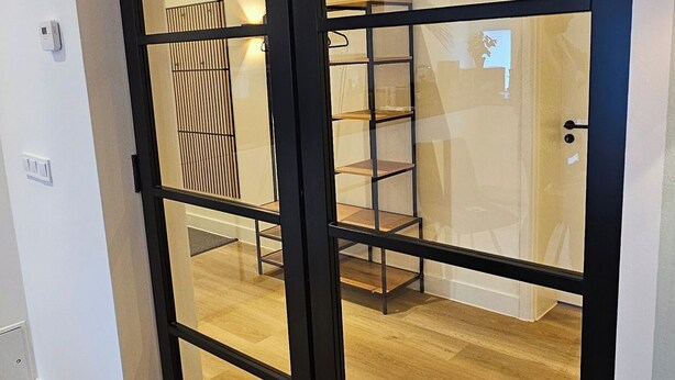 A modern interior with a sliding glass door leading to a room with a wooden floor and a metal shelf unit.