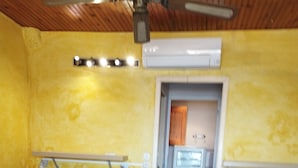 Una habitación con dos camas, ventilador de techo, aire acondicionado y una puerta que da a otra habitación.