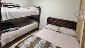 Een kamer met twee stapelbedden, een enkel bed, een plafondventilator en een raam met gordijnen.