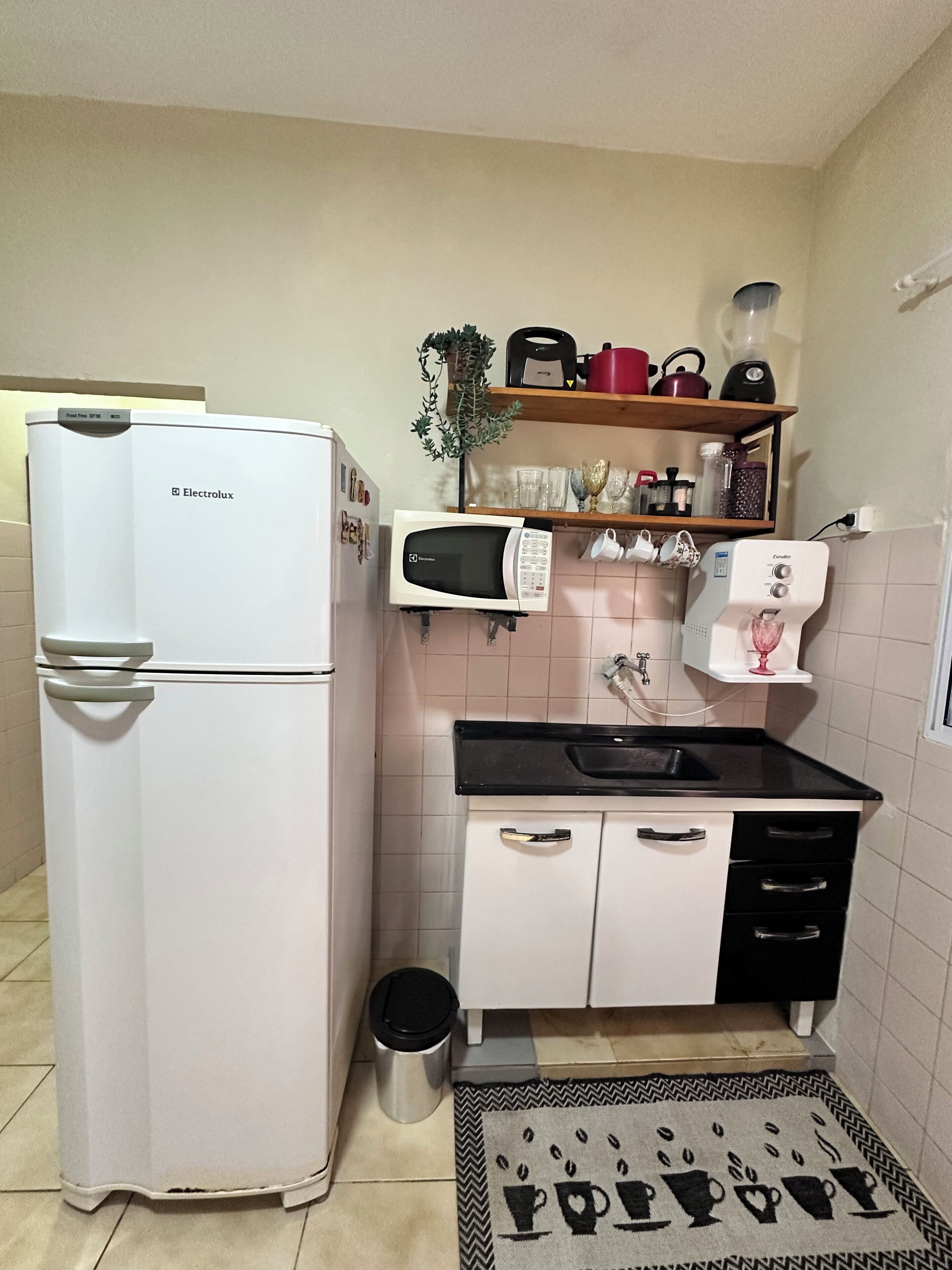 A compact kitchen with a refrigerator, microwave, coffee maker, and a small trash bin.