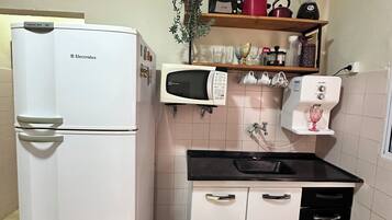 A compact kitchen with a refrigerator, microwave, coffee maker, and a small trash bin.