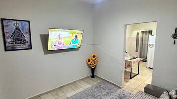 Una sala de estar con televisor, ventilador de techo, alfombra gris, sofá y una mesita con un jarrón de girasoles.