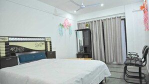 Une chambre d’hôtel équipée d’un lit, d’un bureau, d’une chaise, d’un ventilateur de plafond et de rideaux.