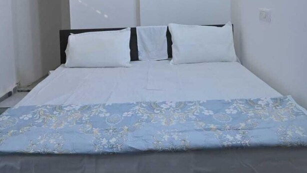 Une chambre à coucher avec un lit, des murs blancs, un ventilateur de plafond et un motif floral sur le mur.