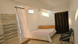 Une chambre à coucher comprenant un lit, une chaise, un bureau, un ventilateur de plafond et une fenêtre avec des rideaux.