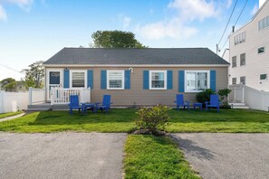 A two-story house with a front porch, blue shutters, and a small lawn with four blue chairs. - Sea Glass (Wells)