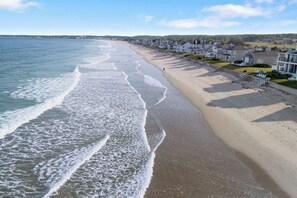 Une plage avec des vagues, une rangée de maisons et un ciel dégagé.