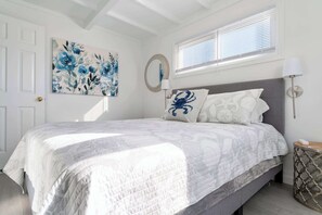 Une chambre à coucher avec un lit, un miroir fixé au mur, une lampe de chevet et une fenêtre avec des stores.