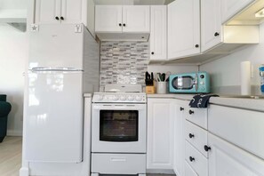 A kitchen with white cabinets, a white refrigerator, a white oven, and a teal microwave. - Sea Glass (Wells)