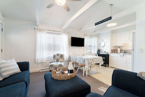 A living room with a sofa, ottoman, and a dining area with a table and chairs. - Sand Dollar (Wells)