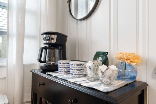 A coffee maker, mugs, a vase with flowers, and a Starbucks bag on a table. - Sand Dollar (Wells)