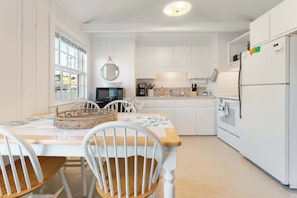 A compact kitchen with white cabinetry, a dining table with chairs, a microwave, and a refrigerator. - Sand Dollar (Wells)
