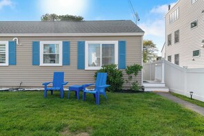 A single-story house with a front porch, a small lawn, and two blue chairs. - Sand Dollar (Wells)