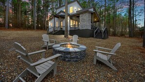 A modern cabin with a stone fire pit surrounded by Adirondack chairs, set in a forested area. - All the Vibes + 2 Story + Shuffle Board + Split Floor Plan + Ride to ATV Trails (Broken Bow)