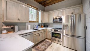 A modern kitchen with white cabinets, stainless steel appliances, and a wooden ceiling. - All the Vibes + 2 Story + Shuffle Board + Split Floor Plan + Ride to ATV Trails (Broken Bow)
