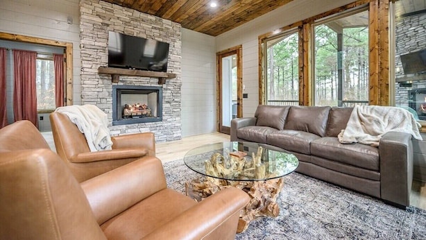 A cozy living room with a stone fireplace, leather sofas, and a glass coffee table. - All the Vibes + 2 Story + Shuffle Board + Split Floor Plan + Ride to ATV Trails (Broken Bow)