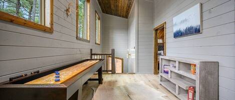 Une pièce chaleureuse avec un plafond en bois, une longue table ornée d’objets bleus et blancs, un tapis en fourrure blanche et une étagère remplie de livres et d’une boîte.