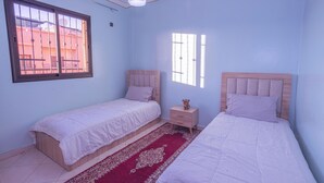 Une chambre avec deux lits simples, une table de chevet, une fenêtre et un tapis rouge à motifs.