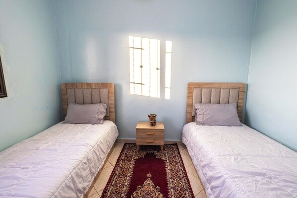 Una camera da letto con due letti singoli, un comodino con una lampada e una finestra con persiane verticali.