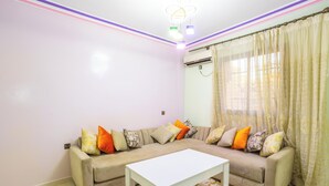 Un salon avec un canapé beige, des coussins colorés, une table basse blanche et un tapis à motifs.