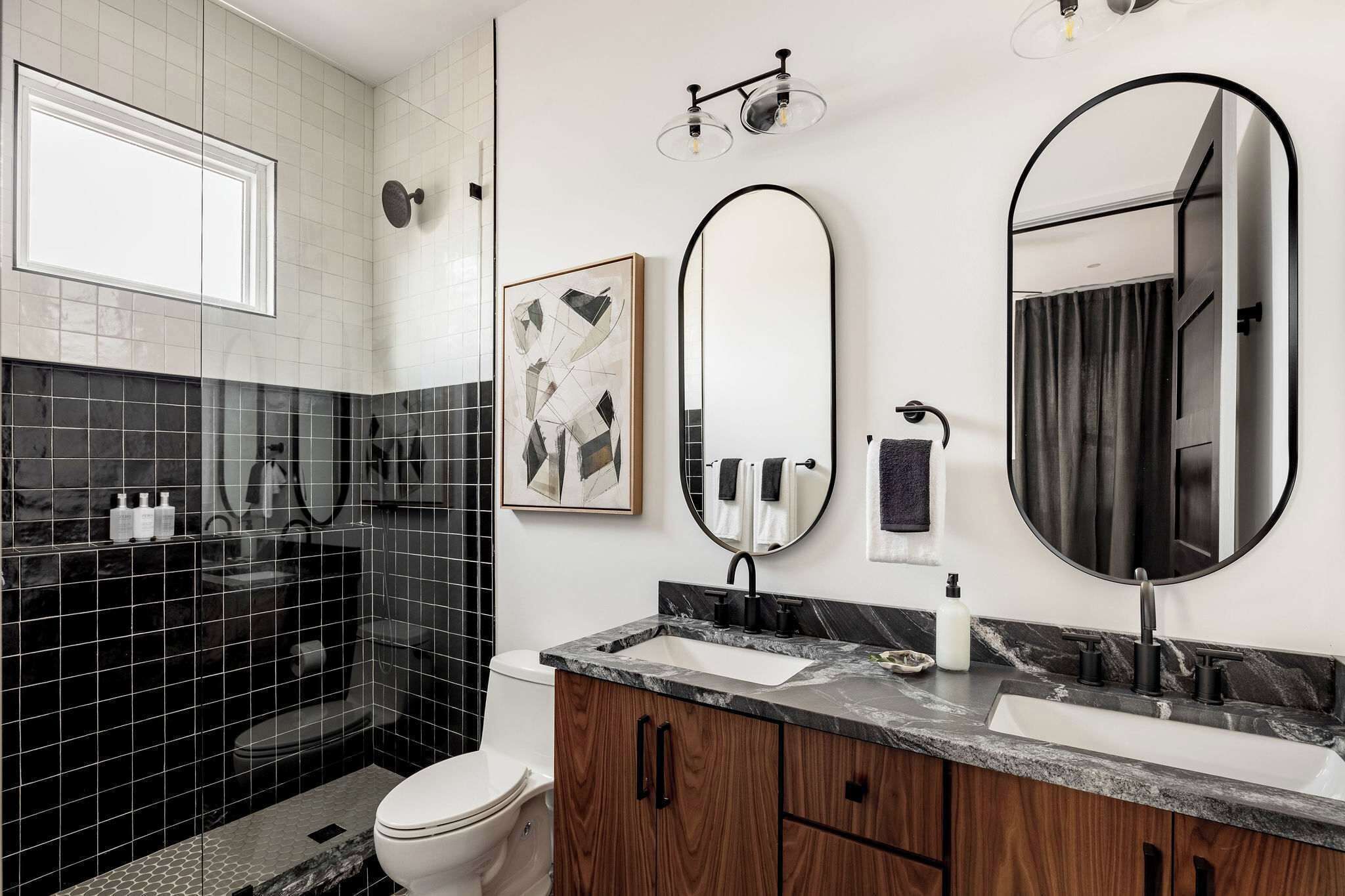 A modern bathroom with a black and white tiled design, a large mirror, and a marble countertop.