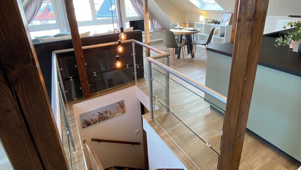 Un appartement de style « loft » avec une mezzanine, des poutres apparentes, une rambarde en verre et une vue sur le paysage urbain.