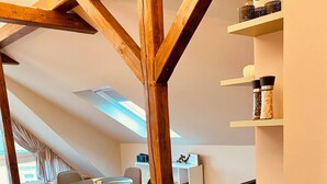 Une cuisine moderne avec des poutres en bois, un coin repas avec une table ronde et des chaises, et une vue sur l’extérieur grâce à une lucarne.