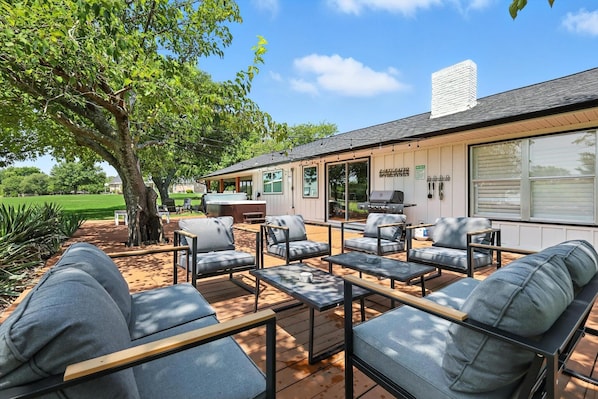 A patio with outdoor seating, a barbecue grill, and a large window overlooking a green landscape.