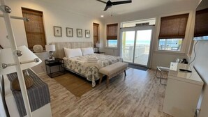 A bedroom with a bed, bench, bedside table, and a view of the beach through a sliding door. - "The Sandy Turtle" Beachfront bungalow, pet friendly Sleeps 8 (Eastpoint)