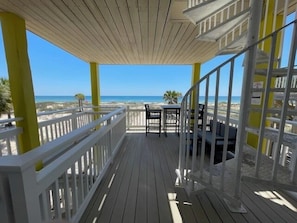 Um deck de madeira com guarda-corpo, uma mesa e cadeiras, com vista para uma praia.