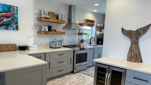 A modern kitchen with grey cabinets, stainless steel appliances, wooden shelves, and a whale tail wall decoration. - "The Sandy Turtle" Beachfront bungalow, pet friendly Sleeps 8 (Eastpoint)