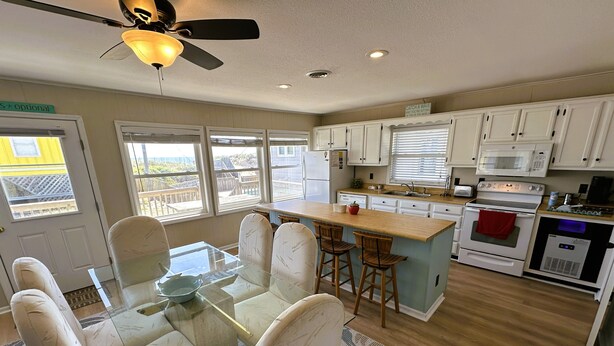 A modern kitchen with a central island, white cabinetry, and a dining area with a glass table and chairs.