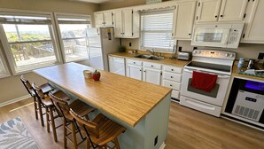 A kitchen with a central island, bar stools, white cabinets, a microwave, an oven, and a dishwasher.