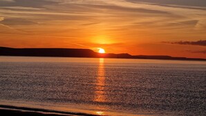Um pôr do sol sobre águas calmas, com uma linha de costa distante.