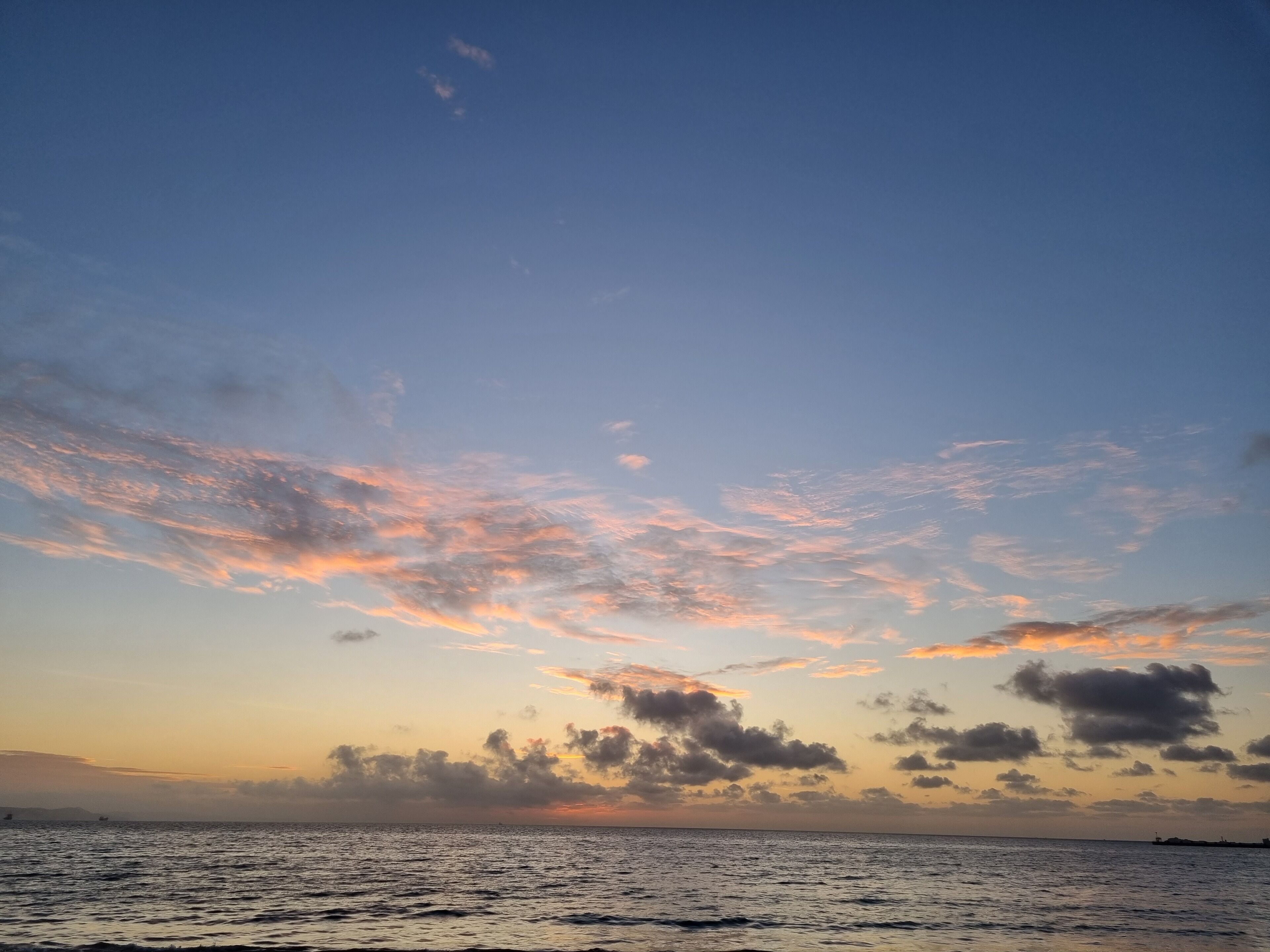 A sunset over a calm sea with a clear sky.